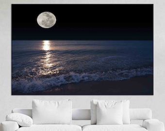 Puede incluir: Una luna llena brilla intensamente sobre un océano oscuro y ondulado con olas rompiendo en la costa arenosa.