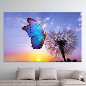May include: A blue butterfly with brown markings sits on a dandelion with dew drops against a colourful sunset sky.