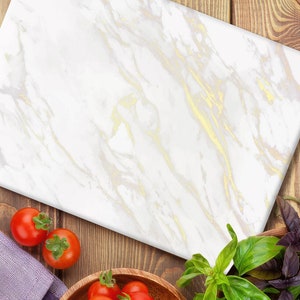 May include: A white marble cutting board with gold veining, surrounded by fresh ingredients like tomatoes, garlic, and basil.