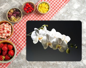 Könnte beinhalten: Ein schwarzes Platzset mit einem aufgedruckten weißen Orchideenblütenmotiv. Das Platzset ist von Schalen mit verschiedenen Snacks und einer rot-weiß karierten Tischdecke umgeben.
