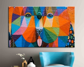 May include: A colorful abstract geometric mural of a dog's face painted on a brick wall. The dog's eyes are large and blue, and its nose is black. The mural is made up of a variety of colors, including orange, blue, green, and pink.