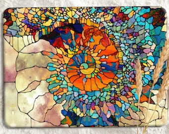 May include: A rectangular decorative item with a stained glass design. The artwork features a spiral pattern in shades of orange, blue, yellow, and green, resembling a nautilus shell. The background is a neutral beige color. Wheat stalks are in the foreground.