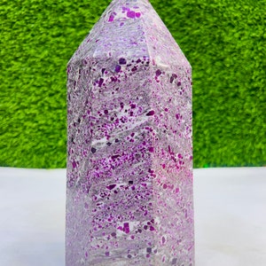 May include: A large, purple and grey crystal point with a hexagonal base. The crystal is made of a natural stone with a speckled pattern.