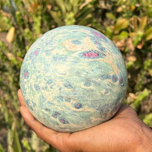 Peut inclure: Une sphère polie de couleur verte et bleue avec des tourbillons et des taches roses et blanches. La sphère est faite d'une pierre naturelle et mesure environ 5 cm de diamètre.