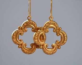 Peut inclure: Boucles d'oreilles dorées en filigrane avec un motif ajouré décoratif. Les boucles d'oreilles présentent un motif orné répétitif avec des formes courbes et de petits accents ronds. Les boucles d'oreilles sont suspendues à de fins crochets dorés.