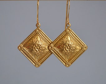 Peut inclure: Une paire de boucles d'oreilles dorées en forme de losange. Chaque boucle d'oreille présente un motif floral en relief au centre et une bordure perlée. Les boucles d'oreilles sont suspendues à de fins crochets incurvés.