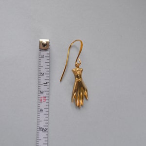 May include: Gold-toned hand-shaped dangle earring with a hook closure. The earring is approximately 2 inches long.