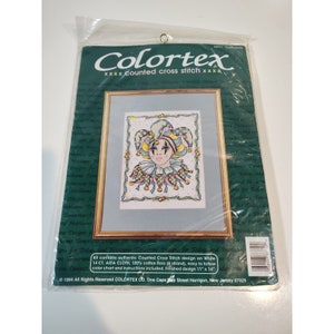 May include: A counted cross stitch pattern featuring a colorful jester with a blue, yellow, and pink hat. The pattern is on white Aida cloth and includes instructions. The finished design is 11 inches by 14 inches.