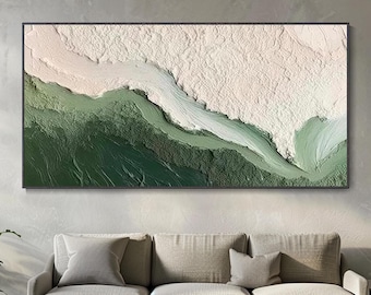 May include: Abstract textured wall art in a black frame. The artwork features a landscape design with shades of green, white, and beige. The painting is displayed above a gray sofa with pillows, creating a modern living room aesthetic.