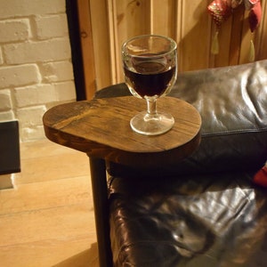 May include: A wooden side table with a black metal pipe leg and a round top. The table is next to a brown leather sofa and a glass of red wine is on the table.