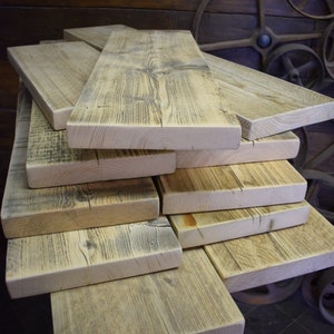 Op de afbeelding: Een stapel gerecyclede houten planken, elk met een uniek nerfpatroon en een verweerde, rustieke uitstraling. De planken zijn in een verspringende stapel gelegd, wat een visueel aantrekkelijk beeld cre&euml;ert.