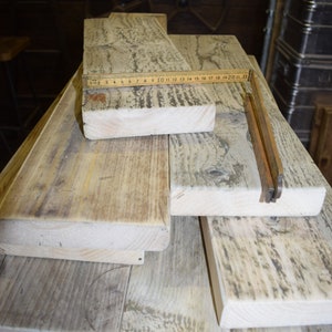 May include: A stack of reclaimed wood planks, some with a weathered gray finish, others with a natural wood color. A wooden ruler is placed on top of the planks, with the numbers 1 through 22 visible.