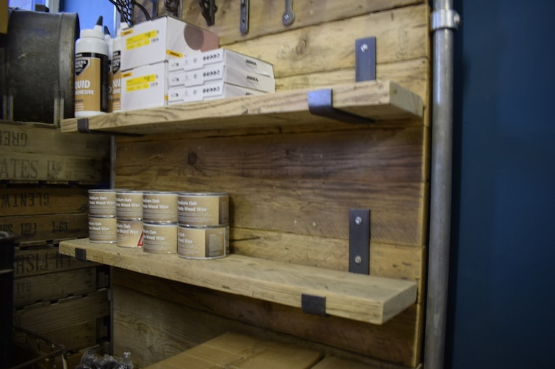 May include: Rustic wooden shelves with metal brackets, mounted on a reclaimed wood wall. The shelves are filled with various items, including cans of wood wax and boxes of supplies.
