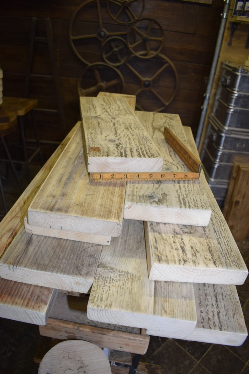 May include: A stack of reclaimed wood planks, some with a weathered gray finish, others with a natural wood color. A ruler is placed on top of the planks, measuring 8 inches.