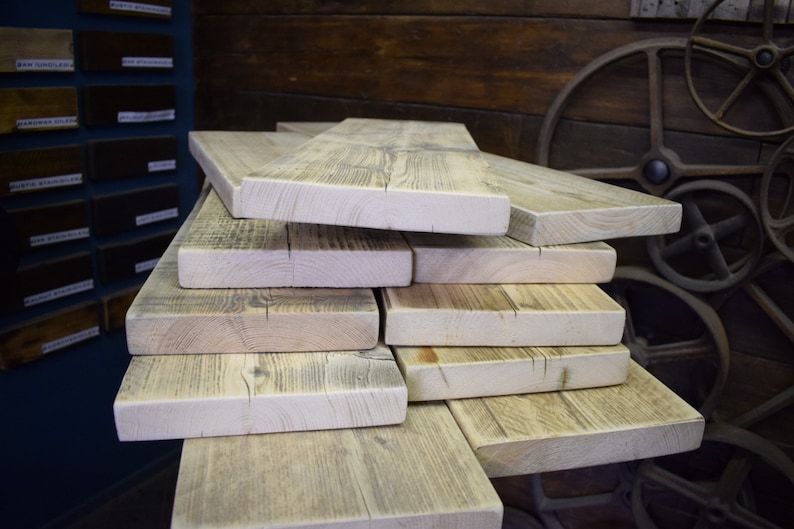 Op de afbeelding: Een stapel gerecyclede houten planken, die de natuurlijke nerf en knoesten van het hout laten zien. De planken zijn verweerd en hebben een lichtgrijze afwerking.