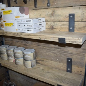 May include: Three wooden shelves with metal brackets, mounted on a rustic wood wall. The shelves are filled with various products, including bottles of liquid adhesive, boxes of sandpaper, and cans of wood wax.