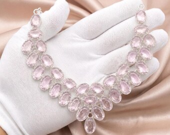 May include: A silver necklace featuring multiple oval-shaped, faceted light pink gemstones arranged in a tiered, V-shaped pattern. The stones are set in polished silver metal settings, creating a symmetrical design that tapers toward the center.