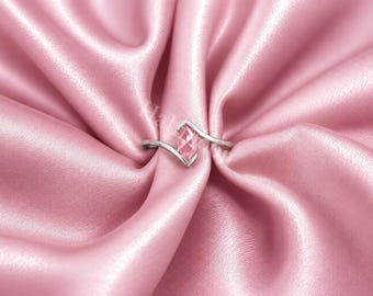 May include: A silver-toned bypass ring featuring a marquise-cut pink gemstone at the center. The band has a sleek, polished finish and curves around the stone, which is set in a V-shaped metal frame. The ring is displayed on a soft pink fabric.