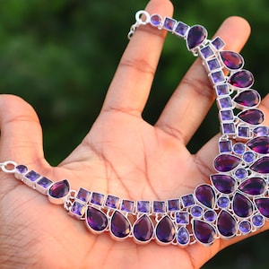 Puede incluir: Un collar de plata con un diseño de piedras preciosas de amatista púrpura. El collar presenta una variedad de formas de amatista, incluyendo gotas y cuadrados.