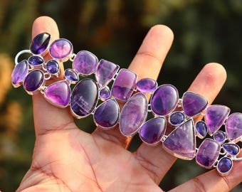 May include: A silver bracelet featuring a cluster of amethyst gemstones in various sizes and shapes. The bracelet is crafted with a silver chain and has a clasp fastening.