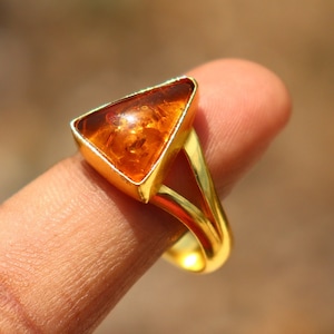 May include: A gold ring featuring a triangular amber gemstone. The ring has a simple design with a split band.