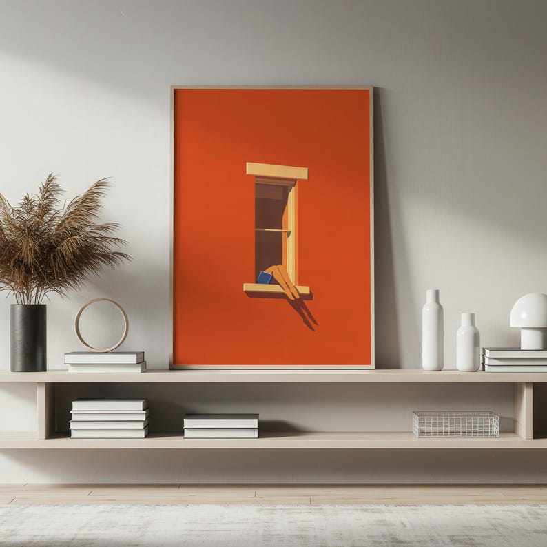 May include: A framed art print featuring a minimalist illustration of a person relaxing in a window. The artwork has a vibrant orange background with a wooden window frame. The person is wearing blue shorts. The artwork is displayed on a shelf.