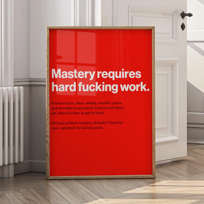 Puede incluir: Un p&oacute;ster rojo enmarcado con texto blanco que dice "Mastery requires hard fucking work". Texto adicional debajo indica el tiempo que se tarda en lograr el dominio. El p&oacute;ster est&aacute; en un marco de madera y se apoya contra una puerta blanca.