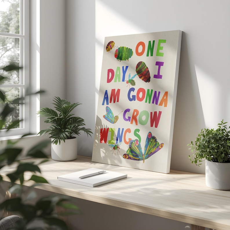 Pu&ograve; includere: Una stampa su tela con la scritta "ONE DAY I AM GONNA GROW WINGS" in lettere colorate. L'opera d'arte include illustrazioni di bruchi, farfalle e altri insetti. La stampa &egrave; esposta su una scrivania di legno con piante e un quaderno.