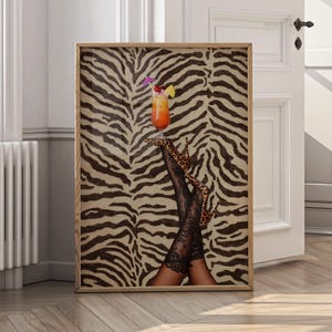 Könnte beinhalten: Gerahmter Kunstdruck mit einem Cocktail mit dekorativem Schirmchen, Kirschen und einer Zitronenscheibe. Der Cocktail balanciert auf Beinen mit schwarzen Spitzenstrümpfen und Leoparden-High Heels, vor einem zebraartig gestreiften Hintergrund.
