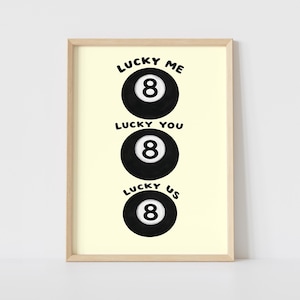 Puede incluir: Impresión enmarcada con tres bolas negras de billar con el número 8 en blanco. Encima de cada bola están las palabras "Lucky Me", "Lucky You" y "Lucky Us". El fondo es amarillo claro, el marco es de madera clara.
