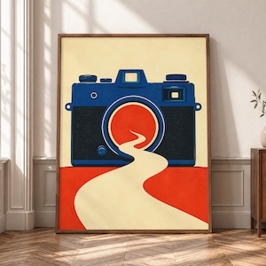 May include: A rectangular wall art print featuring a dark blue camera centered against a cream background. The camera lens is a solid red circle, from which a winding cream-colored path flows downward onto a solid red rectangular base.