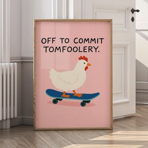 May include: A framed print with a pink background shows a white chicken on a blue skateboard. The text at the top reads "OFF TO COMMIT TOMFOOLERY." The chicken has a red comb and orange beak. The frame is a light brown colour.