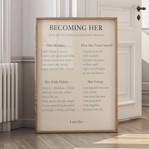 May include: A framed print with the text "BECOMING HER" in a serif font. The print includes affirmations about mindset, daily habits, and energy. The frame is a light wood color, and the print is displayed in a room with a white door.