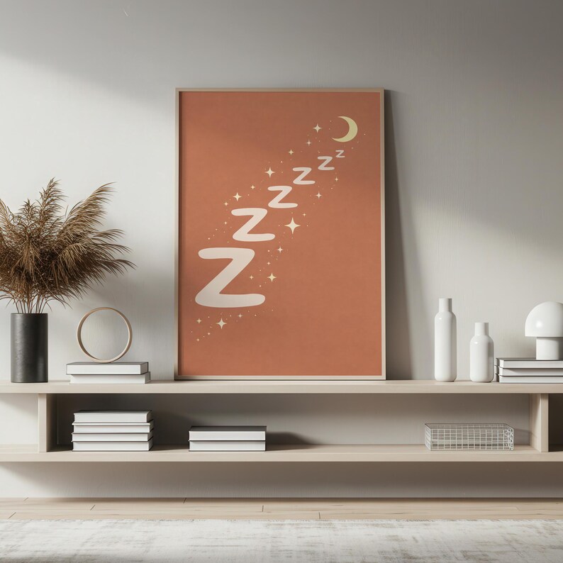 May include: A framed art print with a terracotta background features the word "Zzz" in a whimsical font, along with a crescent moon and stars. The artwork is a decorative piece for a bedroom or nursery.