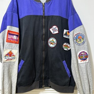 May include: A vintage baseball bomber jacket in black, blue, and grey. The jacket has several patches with text including "1995 World Series" and "Arizona". It features a zip-up front and grey sleeves.
