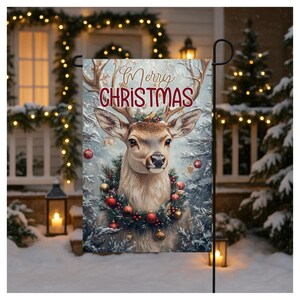 May include: A garden flag featuring a deer with antlers, adorned with a wreath of red and gold ornaments. The words "Merry Christmas" are written across the top. The background shows a snowy scene with Christmas lights.