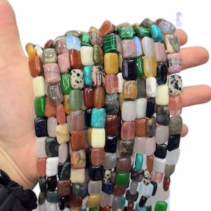 May include: A collection of rectangular gemstone beads in a variety of colours and patterns, including green malachite, blue turquoise, spotted dalmatian jasper, translucent opalite, goldstone, and various shades of quartz, arranged in multiple strands.