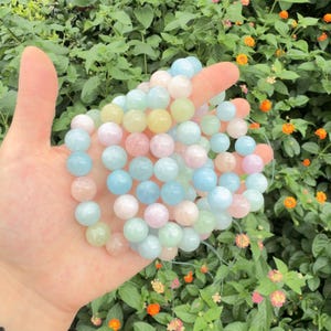 May include: A strand of smooth, round gemstone beads in soft pastel shades of light blue, pale pink, mint green, and creamy yellow. The beads are polished and translucent, strung together on a thin, flexible cord, creating a delicate, multi-colored accessory.