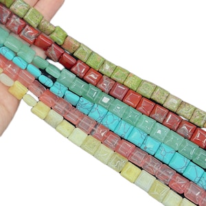 May include: Multiple strands of square-shaped beads in various colors including olive green, deep red, light mint green, bright turquoise with dark veining, translucent pink, and pale yellow, all arranged in parallel rows on a white background.