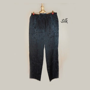 May include: Black silk pants with a floral pattern hanging on a wooden hanger. The fabric has a subtle sheen.