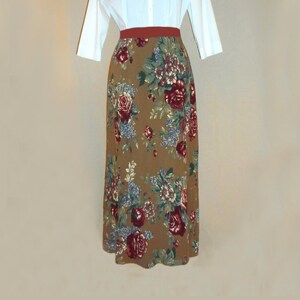 May include: A long brown skirt with a floral print featuring red, blue, and white flowers. The skirt has a brown waistband with a thin red band.