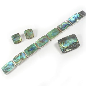 May include: A set of abalone shell jewelry, including a bracelet, a brooch, and a pair of earrings. The jewelry is made of silver and features iridescent abalone shell in shades of green, blue, and gold.