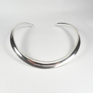 May include: A silver choker necklace with a smooth, curved design.