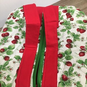 May include: A red and green quilted tote bag with a zipper closure and strawberry print. The bag has two red handles.