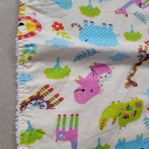 May include: White fabric with a colorful pattern of animals and plants. The animals include a pink elephant, a blue elephant, a brown giraffe, and a green dinosaur. The plants are green and yellow.