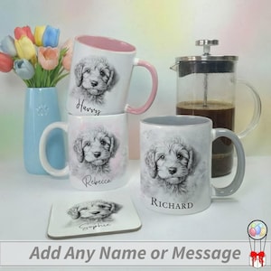 May include: White ceramic mugs with a puppy portrait and personalized names. One mug has a pink interior and handle, another has a gray handle. A matching coaster is also present. A blue vase with tulips and a French press are in the background.