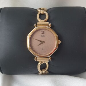May include: A gold-toned Seiko Quartz wristwatch with a rose gold face and a linked bracelet. The watch face has Roman numeral hour markers and a small second hand.