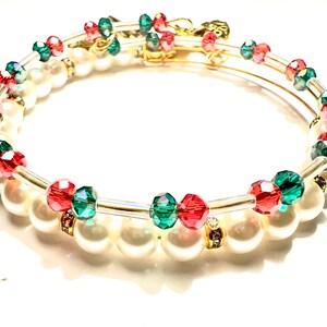 May include: A pair of gold bangle bracelets with red and green crystal beads and white pearls.