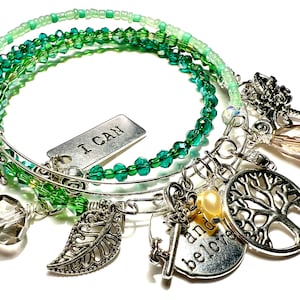 May include: A silver charm bracelet with green glass beads and charms that say "I can" and "and believe". The bracelet also features a charm of a tree, a leaf, a key, and a crystal.