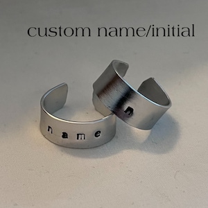 Può includere: Due anelli in metallo argentato con le parole "name" e "n" incise. Anelli personalizzati con nome o iniziale.